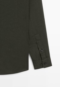 Donkergroen shirt met lange mouwen en een gladde textuur, met zwarte knopen op de manchetten en een gebogen zoom.