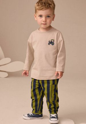 Beige Langarmhemd mit Traktor-Stickerei, grün und marineblau gestreifte Hose und blaue Turnschuhe. Glatter Stoff, lockere Passform.