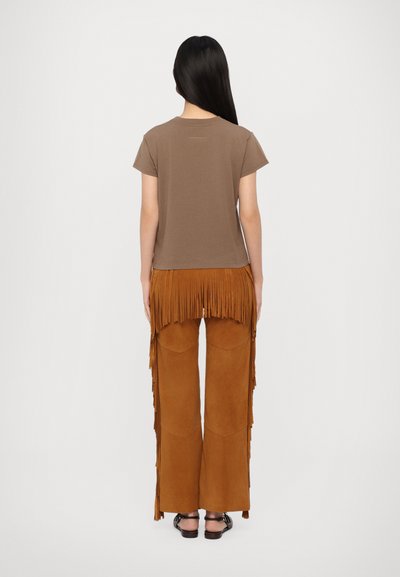 Bruine korte mouwen t-shirt gecombineerd met dijlange, franjes, camelkleurige suède broek met wijde pijpen en een gladde textuur.