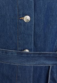 Denimjack met een donkerblauwe kleur, zilveren knoopdetails en een bijpassende riem. De stof heeft een gladde textuur met zichtbare stiksels.