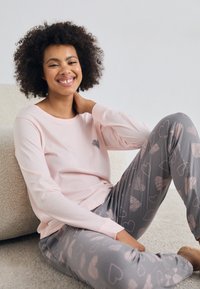 Ljust rosa långärmad topp med en liten snäcka grafiskt tryck, matchad med grå byxor med ett hjärtformat mönster i ljust rosa och en avslappnad passform.