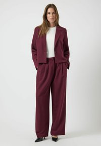 Blazer entallado burdeos con pantalones de pierna ancha a juego. Tejido suave, hombros estructurados, cierre frontal con botones y bolsillos laterales.