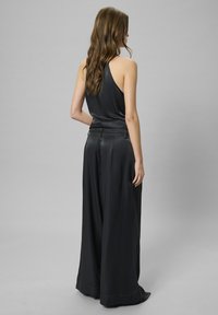 Top nero senza maniche con una texture liscia, abbinato a pantaloni a gamba larga caratterizzati da un taglio sartoriale e una leggera lucentezza, visti da dietro.