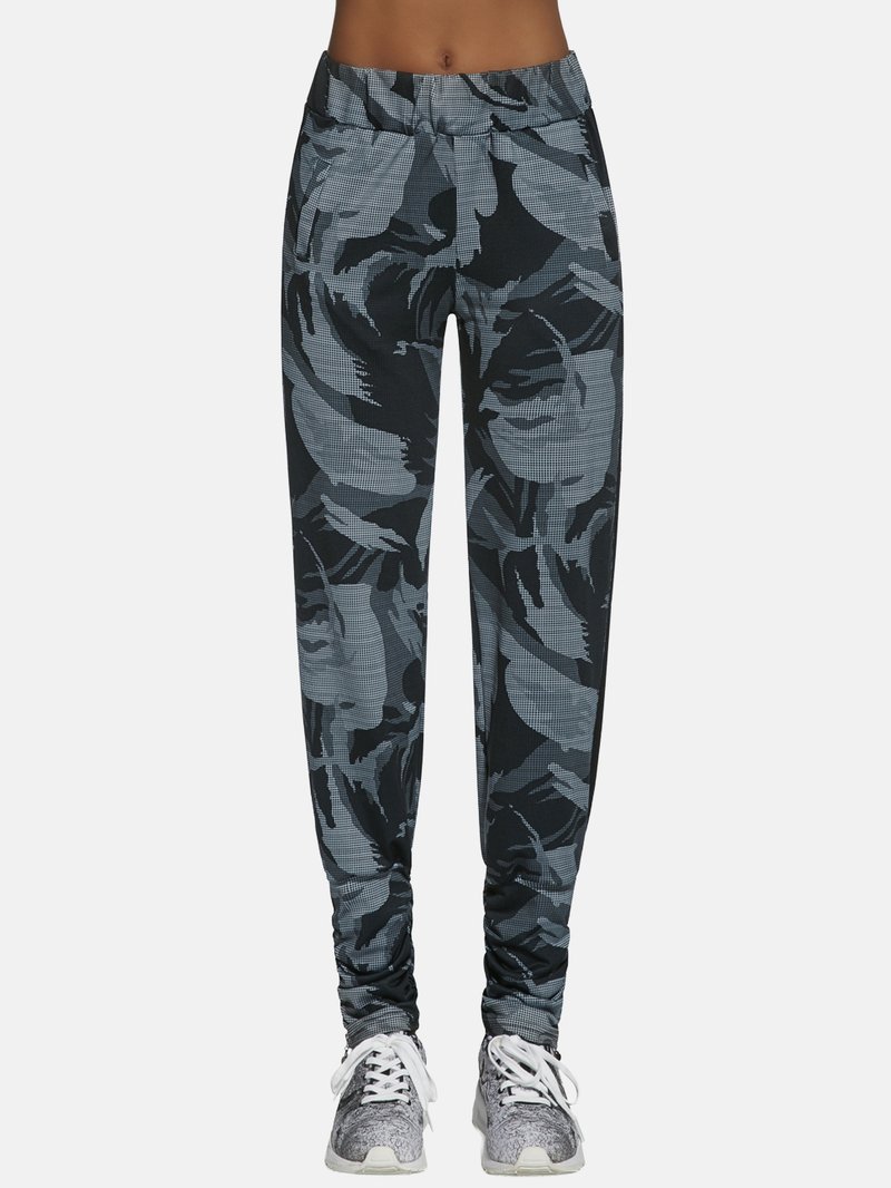 Czarno-szare spodnie dresowe z wzorem, z elastycznym pasem, ozdobione motywem liści i zwężane ku dołowi, zestawione z szarymi trampkami.