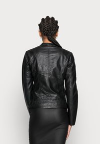 Veste en cuir noir avec un design ajusté, présentant des surpiqûres et un dos texturé, vue de l'arrière avec des manches longues.