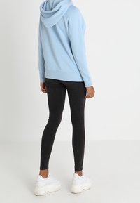 Hellblaues Kapuzensweatshirt, Baumwollmischung, lockere Passform. Kombiniert mit schwarzen Skinny-Jeans und weißen, klobigen Sneakers.