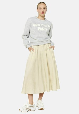 Sweatshirt gris avec "MON CHÉRI PARIS" en blanc, associé à une jupe midi fluide couleur crème et des baskets blanches avec des accents marron.