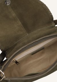 Olijfgroen suède handtas met een gestikte rand, voorzien van een ritsvak en een beige stoffen voering. Magnetische drukknoopsluiting.