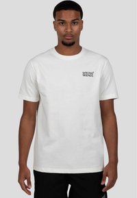 Camiseta de algodón blanca con un logo negro de "WRONG FRIENDS" en el lado izquierdo del pecho. Mangas cortas y un diseño clásico de cuello redondo.