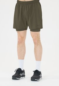 Olivgrüne Sportshorts mit elastischem Bund, aus leichtem Stoff, mit kurzer Länge, kombiniert mit schwarzen Laufschuhen und weißen Socken.
