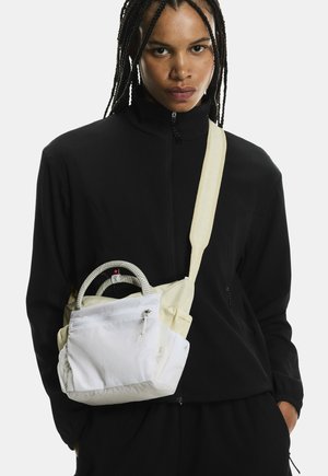Person wearing a black zip-up jacket with braided hair, carrying a white crossbody bag with a front zipper pocket and rope handles.