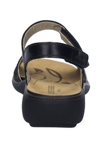 Musta nahkasandaali, jossa on säädettävät hihnat, litteä pohja ja pehmeä beige sisäpohja, jossa on lehtikuvio.
