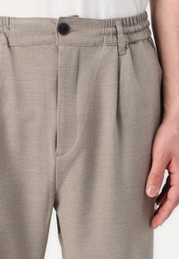 Ljust grå, texturerad tygbyxor med knappstängning och elastisk midja, med veck och sidofickor.