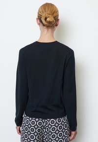 Pull en maille bleu marine à manches longues avec un col rond et des poignets côtelés. Porté avec un pantalon à motifs floraux bleus et bruns.