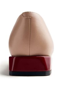 Chaussure en cuir beige avec un bout rond et un talon bloc rouge brillant. Le talon est de forme carrée, ajoutant une touche moderne au design.