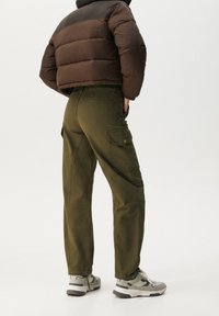 Brun vadderad jacka, olivgröna cargobyxor med fickor och gråa sneakers. Tyget är mjukt och byxorna har en lös passform.