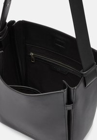 Czarna skórzana torba na ramię o gładkim wykończeniu, wyposażona w zamykaną na zamek wewnętrzną kieszeń oraz otwartą komorę, prezentująca minimalistyczny design.
