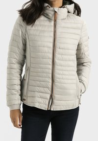 Lysegrå quiltet jakke med høj krave, lynlås foran og sidelommer. Har en diskret tekstur og brune detaljer på lynlåse.