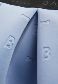 Světle modrá látka s embosovanými vzory "B" a motýlků, s kontrastním černým pasem. Navrženo s sklady pro texturu a detail.
