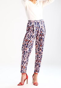 Pantalons à motifs présentant des formes géométriques en marine, rose et orange. Taille haute avec des jambes fuselées, associés à des sandales à talons rouges.