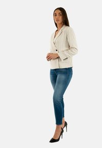 Blazer beige clair à rayures fines avec une coupe ajustée, associé à un jean skinny bleu et des escarpins noirs. Tissu lisse avec des accents de boutons.