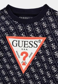 Blau gemusterter Sweatshirt mit einem gerippten Kragen. Enthält ein weißes und rotes Dreieckslogo mit dem Text: "GUESS", "WASHED" und "JEANS."