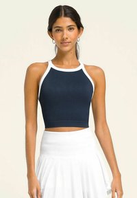 Top corto de canalé en azul marino con ribete blanco, que presenta un cuello alto y un diseño ajustado. Combinado con una falda blanca con pliegues.