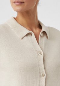 Beżowy sweter z dzianiny z kołnierzykiem, z czterema kremowymi guzikami. Teksturowany materiał o średniej grubości.