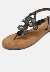 Brown suede sandal with floral appliqué design in black, featuring a toe post and adjustable ankle strap. Soft footbed for comfort.