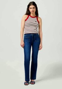 Top de tiras com detalhes em vermelho, combinado com jeans flare azuis. A roupa apresenta um design ajustado e uma textura de tecido suave.