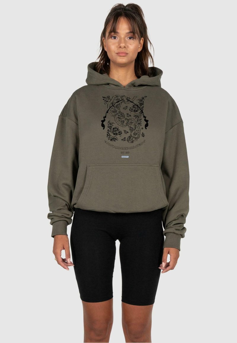 Olive zielony, oversize'owy hoodie z kieszenią z przodu, wyposażony w czarny graficzny wzór kwiatowy oraz tekst „EST. 2015”. Noszony z czarnymi szortami motocyklowymi.