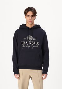 Felpa navy con tasca frontale e cappuccio con lacci. Caratterizzata da un design grafico bianco con "LES DEUX Sporting Goods" e "EST. 2011."