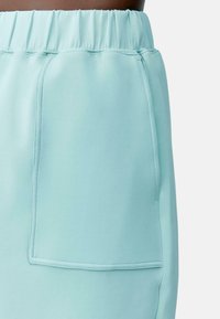 Világoskék sportnadrág elasztikus derékkal, egy oldalsó zsebbel és sima, rugalmas anyaggal.