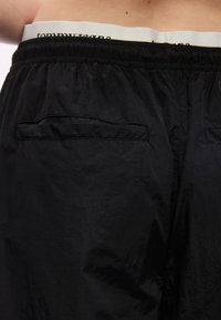 Άνδρας που φοράει μαύρα σορτς με ελαστική μέση και εμφανές λευκό λάστιχο από τα εσώρουχα που ξεχωρίζει πάνω από τα σορτς.