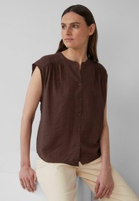 Bruine blouse met korte mouwen en een ronde halslijn, met voor knopen en zachte, gestructureerde stof, gecombineerd met lichte broek.