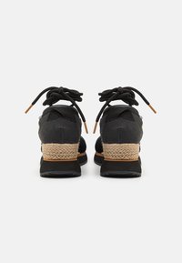 Chaussures noires avec des accents de talon tressés en beige, dotées de lacets ronds et d'un col rembourré. Tissu texturé sur le dessus et semelle en caoutchouc.