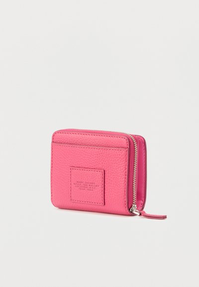Portefeuille compact en cuir rose avec fermeture éclair argentée et une petite pièce cousue embossée des détails de la marque et du style.