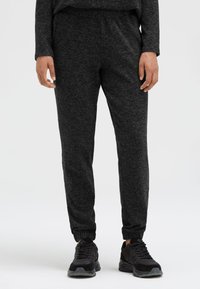 Dunkelgraue Jogginghosen aus weichem Stoff mit elastischem Bund und Bündchen an den Knöcheln, kombiniert mit schwarzen Sportschuhen.