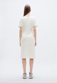 Φόρεμα με κοντά μανίκια και μήκος μέχρι το γόνατο, κατασκευασμένο από λευκό βαμβάκι με πράσινες λεπτομέρειες στο γιακά και τα μανίκια, με εφαρμοστή σχεδίαση.