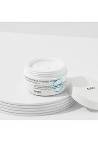 Pot rond blanc de la crème hydratante COSRX Moisture Power Enriched Cream avec du texte bleu et noir. Le couvercle est légèrement entrouvert, révélant une crème épaisse. Surface lisse.