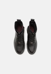 Bottes courtes en cuir noir avec fermeture à lacets sur le devant et fermeture éclair latérale, présentant une finition texturée et une doublure intérieure contrastante rouge.