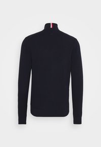 Suéter de punto azul marino con un cuello alto y detalles de rayas rojas y blancas en la parte trasera del escote. Presenta mangas largas y un acabado texturizado.