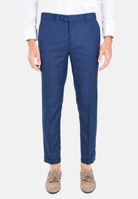 Pantaloni eleganti blu navy in tessuto testurizzato, slim fit, con chiusura anteriore a bottone e passanti per cintura, abbinati a mocassini beige.