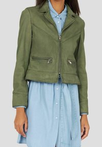 Olivengrøn læderjakke med cropped pasform, lynlåslommer og klapkrave, kombineret med en lys blå chambray kjole.