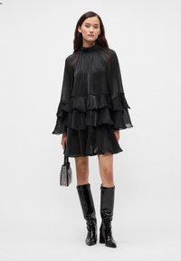 Mustast kihilisest kleidist, millel on pikad varrukad, kõrge kaelus ja voolav kangas. Kandmiseks valitud sädelev must väike kott ning põlveni ulatuvad läikivad mustad saapad.