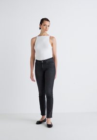 White ribbed tank top paired with high-waisted dark jeans. Model wears black ballet flats. Smooth textures and a fitted silhouette are visible.