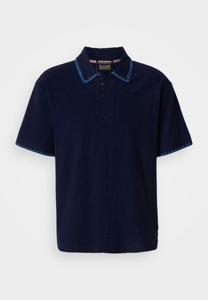 Polo de manga corta color azul marino confeccionado con tela suave, con cuello y puños estampados en contraste azul y cuatro botones en el escote.