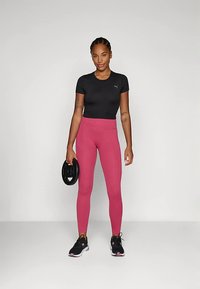 Camiseta negra de manga corta, leggings rosa de cintura alta, sosteniendo una pesa. Zapatillas con detalles en negro, blanco y rosa. Texturas suaves.