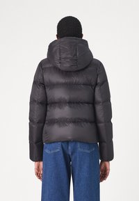 Black puffer jacket with a hood, featuring a quilted design, smooth texture, and elastic cuffs. Paired with wide blue denim trousers.