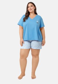 Niebieska koszulka typu V-neck z małym wzorem żaglówki na lewej piersi, w połączeniu z białymi i niebieskimi paskowanymi szortami. Miękka tkanina, luźny krój.